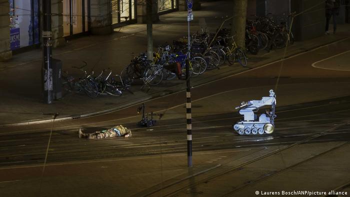 Un hombre camuflado yace junto a un robot policial en la calle.
