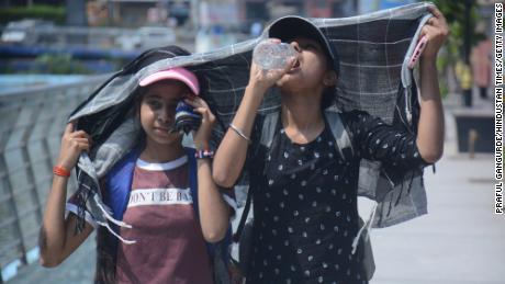 Las niñas se cubren la cabeza mientras caminan y beben agua en el calor abrasador de la tarde de Mumbai.