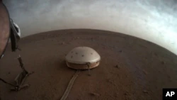 En esta imagen sin fecha puesta a disposición por la NASA el jueves 22 de julio de 2021, las nubes se desplazan sobre el sismómetro SEIS cubierto por una cúpula del módulo de aterrizaje InSight en Marte.