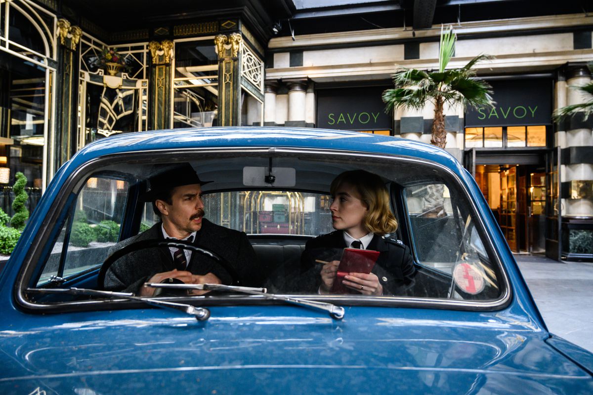El inspector Stoppard (Sam Rockwell) y el agente Stalker (Saoirse Ronan) hablan en un pequeño coche de policía azul fuera del hotel Savoy.
