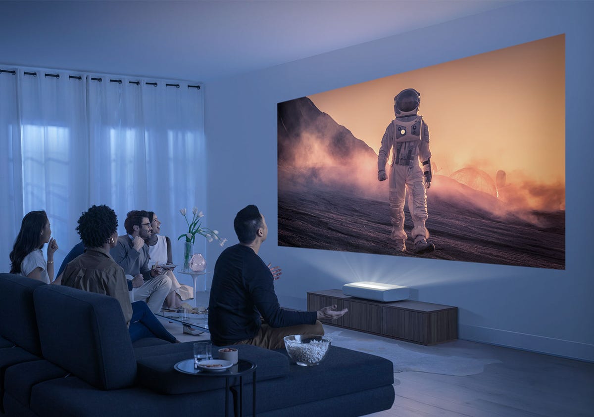 Un salón con varias personas viendo una imagen simulada de un astronauta en la pared creada por el proyector UST.
