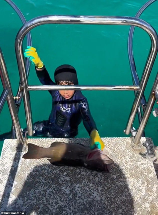 El joven pescador con arpón Manny levanta su pez en la plataforma de buceo detrás del barco