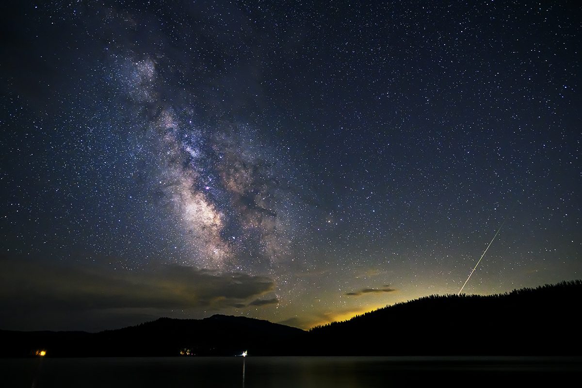 Se representa una lluvia de meteoritos contra un cielo estrellado y un primer plano panorámico