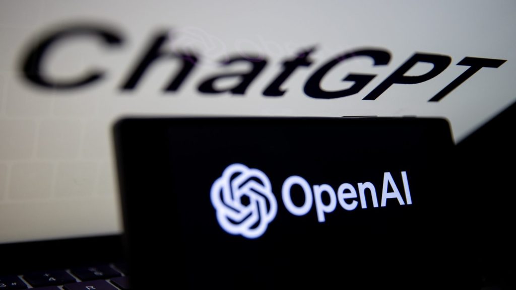 El logotipo de OpenAI se muestra en la pantalla del teléfono móvil frente a la pantalla de la computadora junto con el logotipo de ChatGPT.