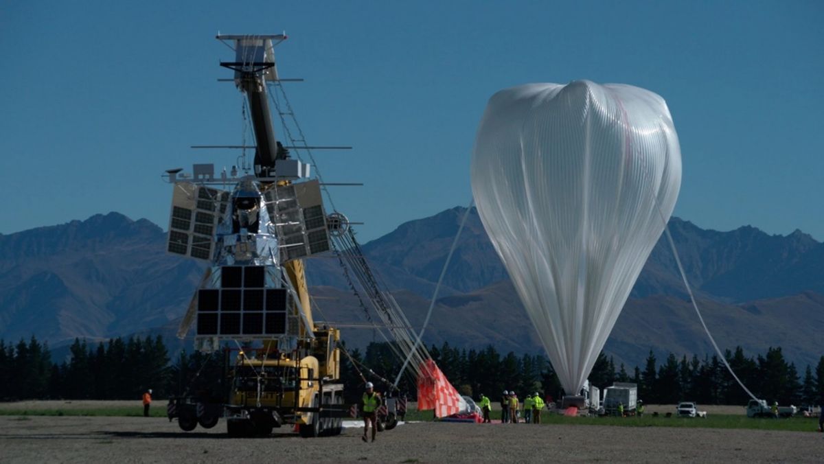 a large white partially inflated balloon rests on the ground, with mountains in the background