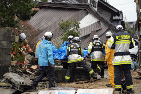 Bomberos y rescatistas cargan un cuerpo, con una sábana azul, recuperado de una casa que se derrumbó debido a un fuerte terremoto en Suzu, prefectura de Ishikawa, el miércoles 3 de enero de 2024. (Foto AP/Hiro Komai)