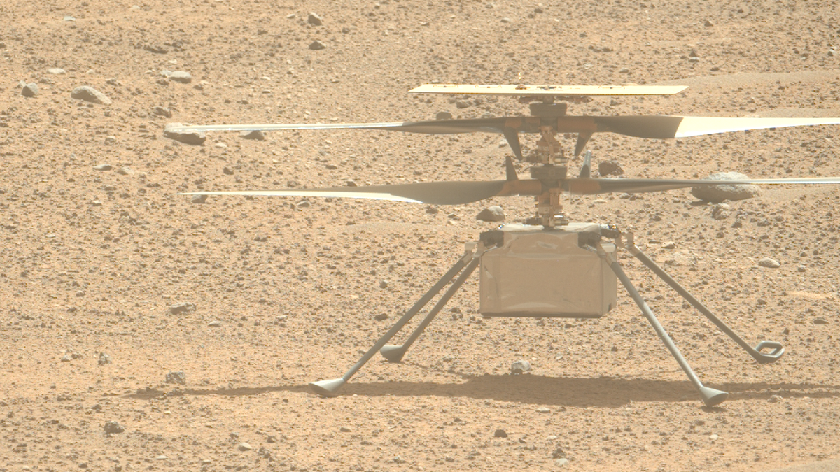 closeup of a four-rotor drone sitting on pebbly red dirt.