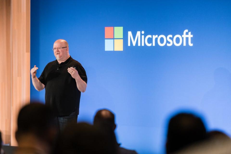 El CTO de Microsoft, Kevin Scott, hace una presentación en el escenario frente a una pared azul con el logotipo de Microsoft.  Las cabezas del público aparecen borrosas en primer plano.